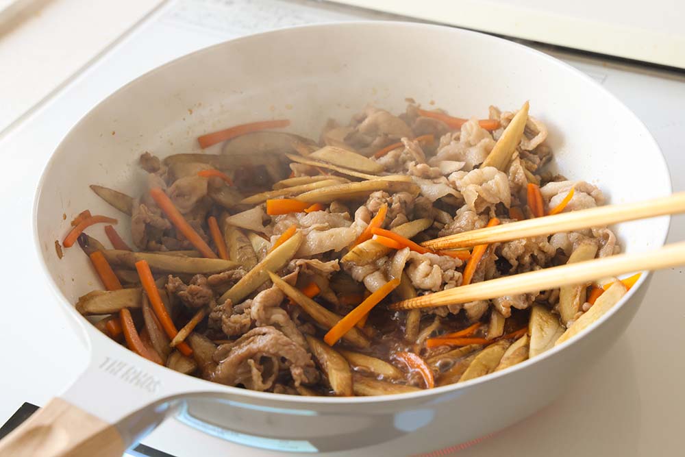 ごぼうと豚肉のおかずきんぴらで調味料を加え炒め煮している写真