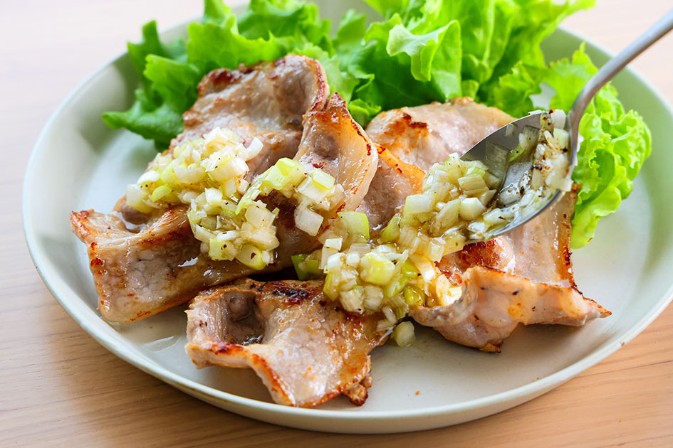 豚肉のねぎ塩だれで、焼いた豚肉にたれをかけている写真