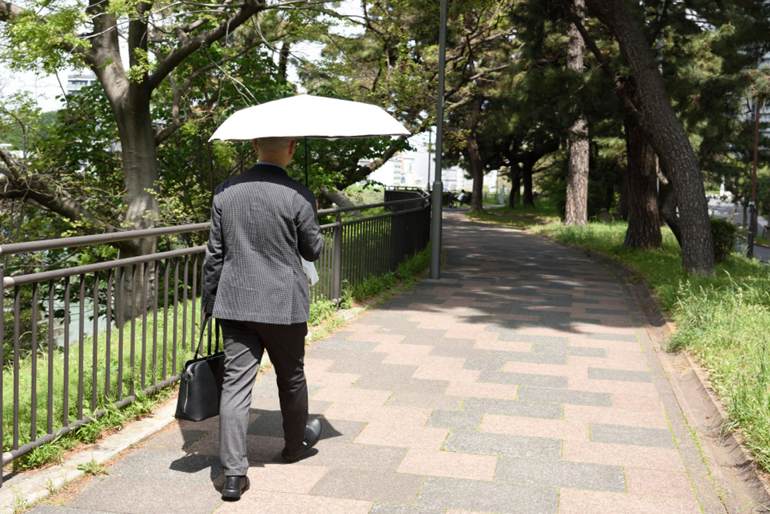 日差しのなか「COOL遮熱 日傘」を差して歩く男性ライター